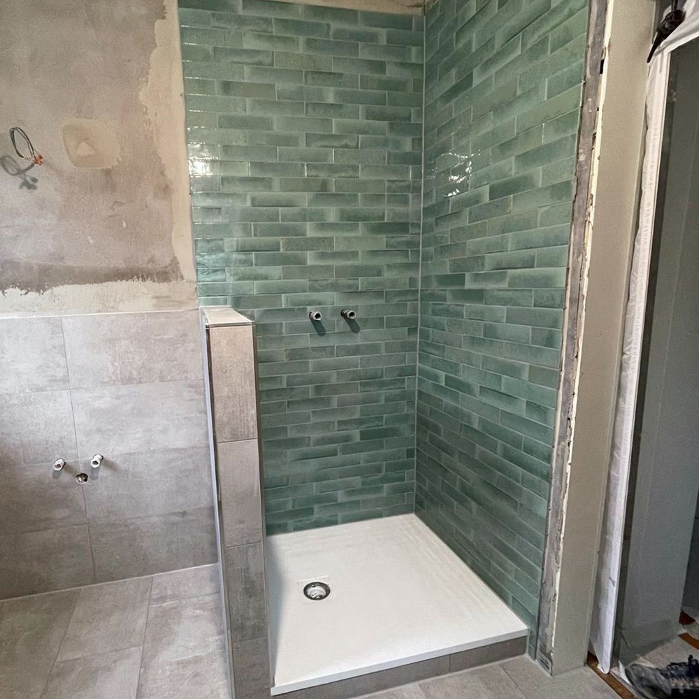 Dusche mit glasierten grünen Metrofliesen und hellem Bodenbelag im Bauzustand