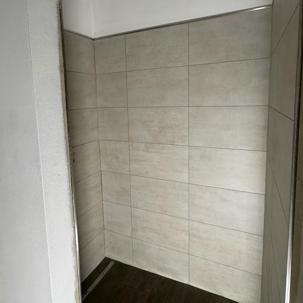 Begehbare Dusche mit dunklem Boden und hellen Wandfliesen vor der Endmontage