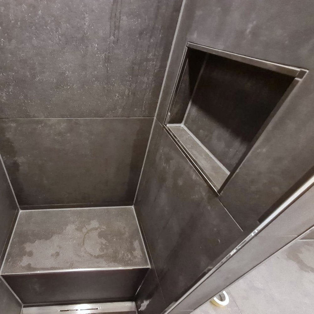 Anthrazitfarbene Dusche mit eingefliester Wandnische und Sitzbank, die Kanten mit Metallprofilen eingefasst