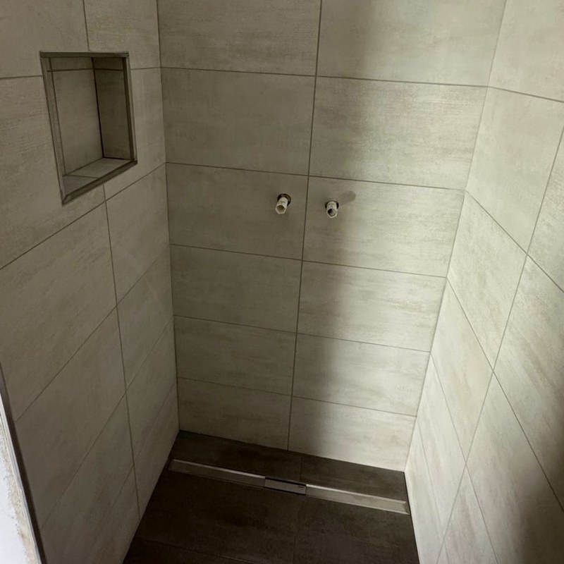 Dusche mit grauen großformatigen Wandfliesen, eingefliester Nische und Duschrinne im dunklen Boden