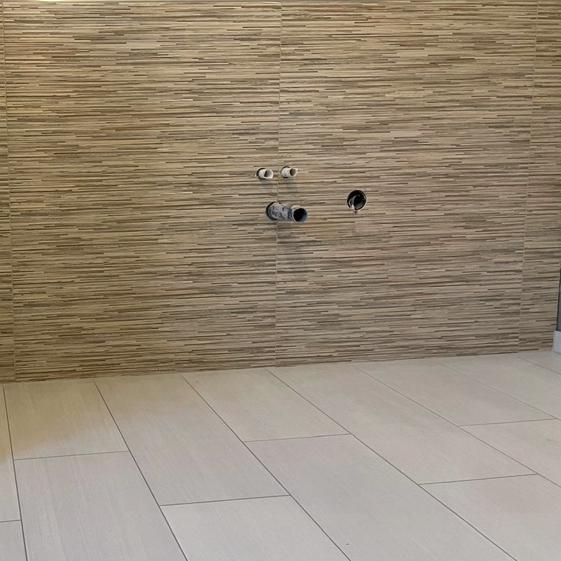 Trennwand mit Abschlussprofil vor einer Wand in Holzoptik, daneben die Anschlüsse für das WC